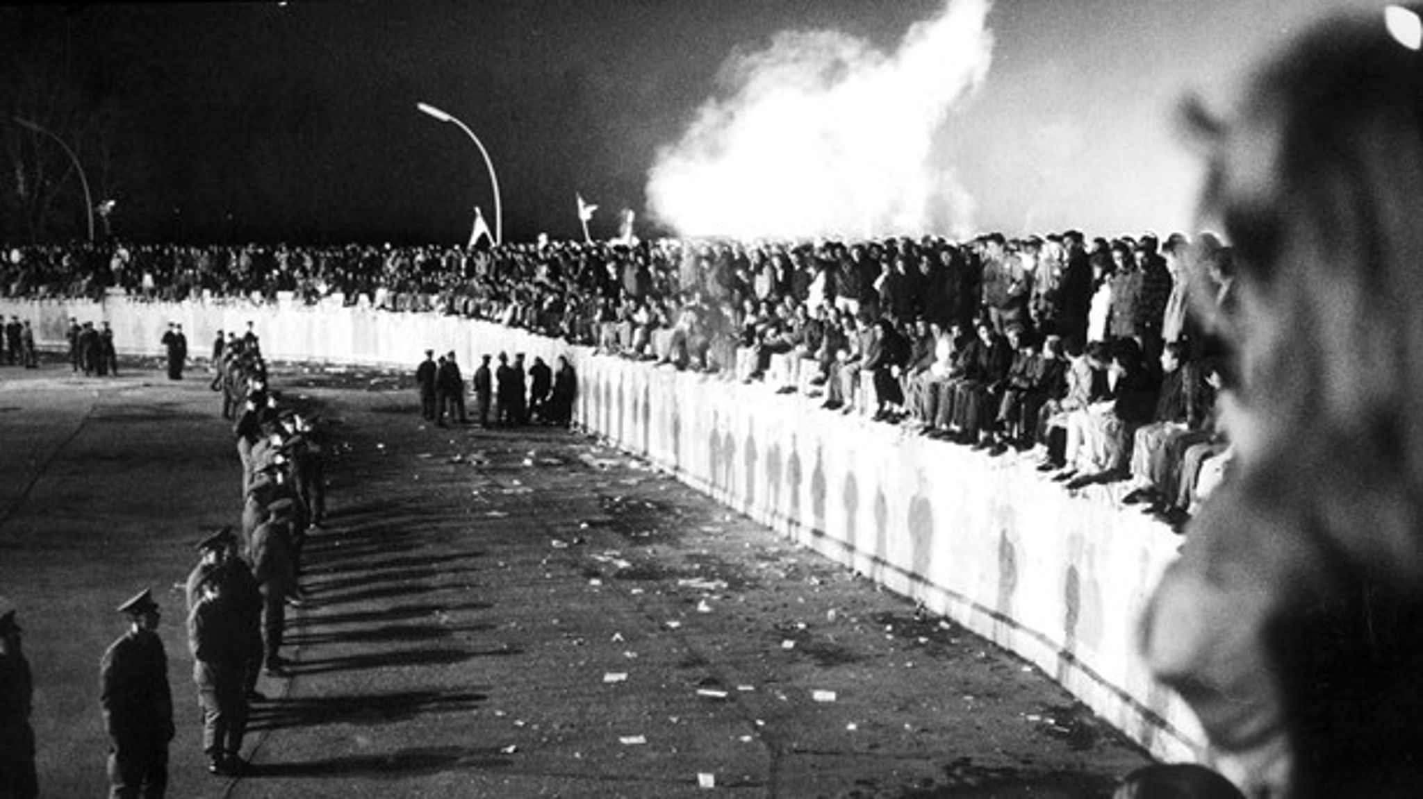 Tusindvis er samlet på Berlinmuren ved Brandenburger Tor i Vestberlin 10. november 1989, dagen efter den østtyske regering åbnede grænsen.&nbsp;På østsiden står politiet klar.