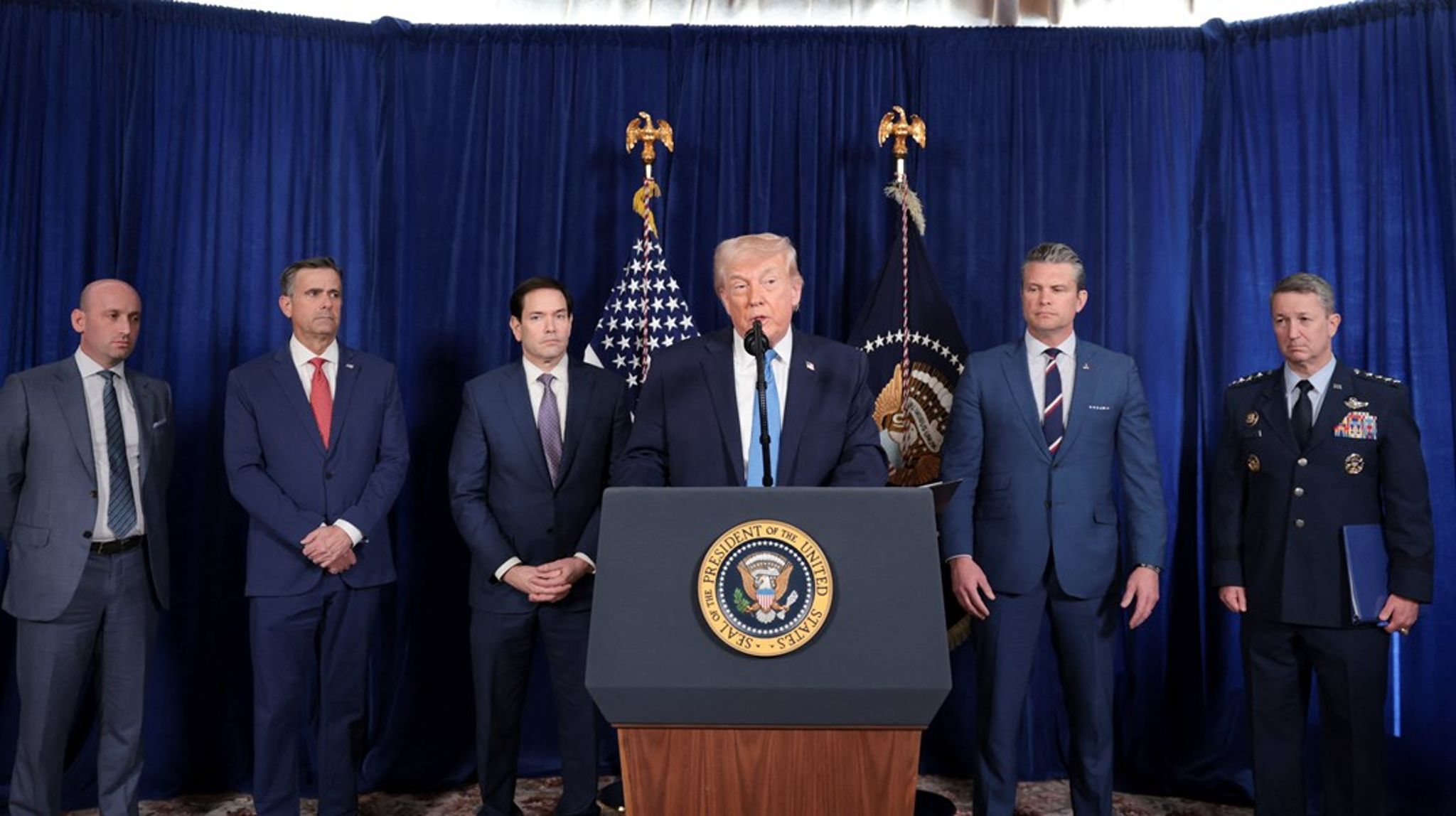 På et pressemøde lørdag vart præsident Donald Trump flankeret af udenrigsminister Marco Rubio til venstre og forsvarsminister Pete Hegseth til højre. Yderst til venstre ses Trump-rådgiveren Stephen Miller, hvis kone senere skrev på sociale medier, at Grønland "SNART" bliver amerikansk.<br><br>