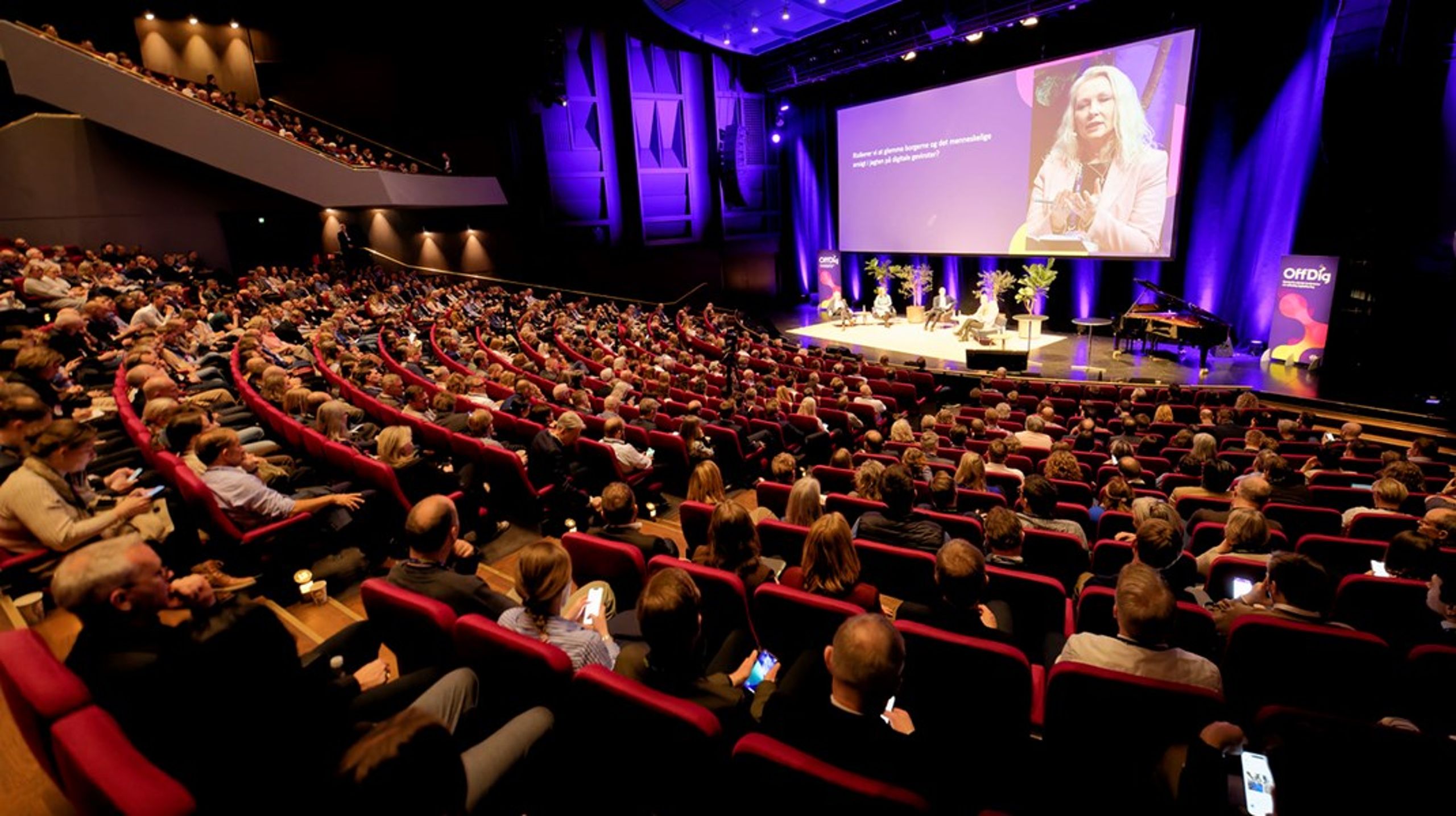 Dina Raabjerg (K) på storskærmen under konferencens åbningsdebat på den store scene i Musikhuset Aarhus, mens publikum sender spørgsmål via konferencens app.
