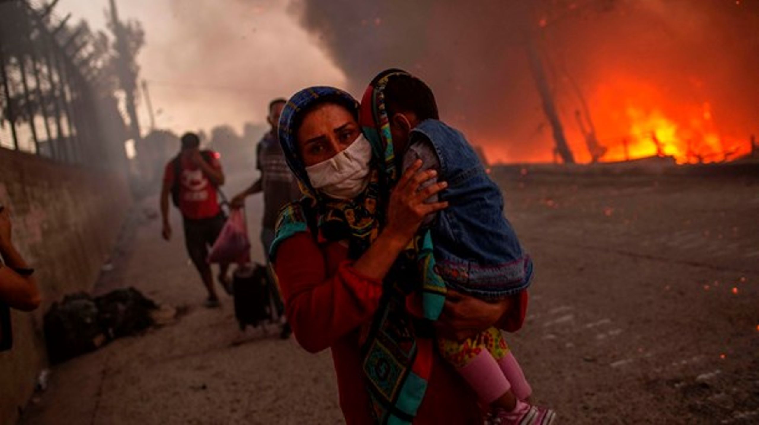 En kvinde bærer sit barn forbi flammerne i Moria-lejren, hvor en stor brand brød ud 9. september. Der boede 12.000 i lejren, der brændte ned til grunden.