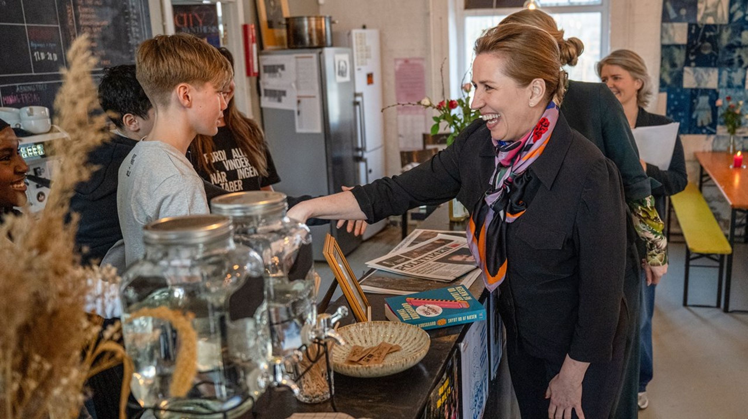 Mette Frederiksen hilser på unge på arbejde på en café. Regeringen, Reformkommissionen og ikke mindst arbejdsgiverorganisationerne vil have flere unge til at tage et fritidsjob.