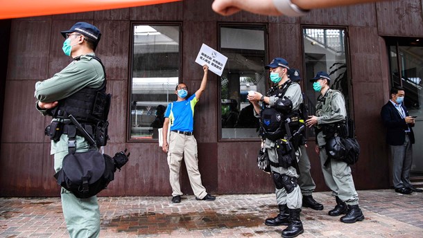 Politibetjente i Hong Kong står vagt nær ​​en prodemokrati-protestant, som sammen med en gruppe andre har fået en bøde for at overtræde de sociale distanceregler under covid-19. Coronavirussen har mange steder i verden fået civilsamfundets råderum til at skrumpe.